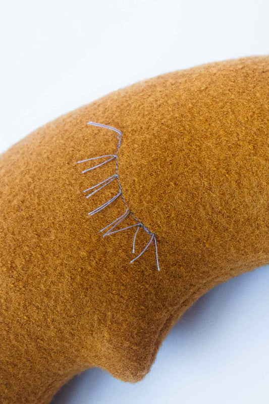 Detail des kleinen Mondkissens in Goldgelb mit liebevollen Wimpern in Flieder für Babys und Kinder