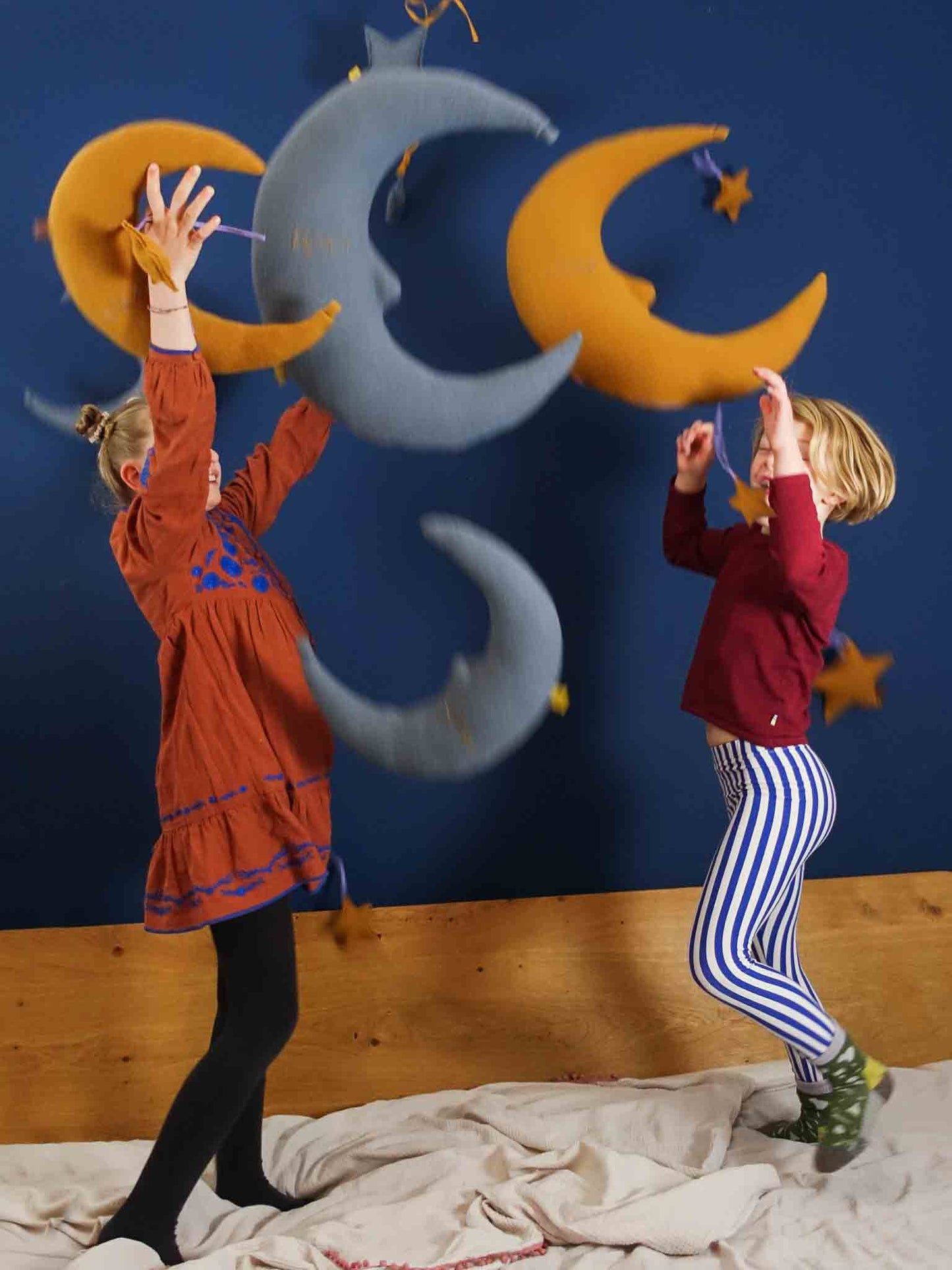 blaue und gelbe Kissen in Mond- und Sternform werden von zwei Kindern im Spiel nach oben geworfen