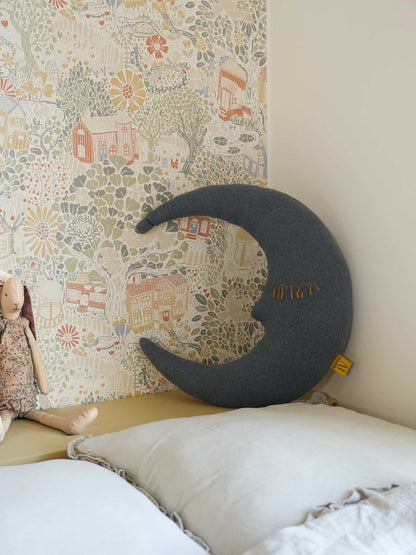 blaues Kuschelkissen in ondform in Kinderzimmer vor verspielter Tapete hinter einem Bett