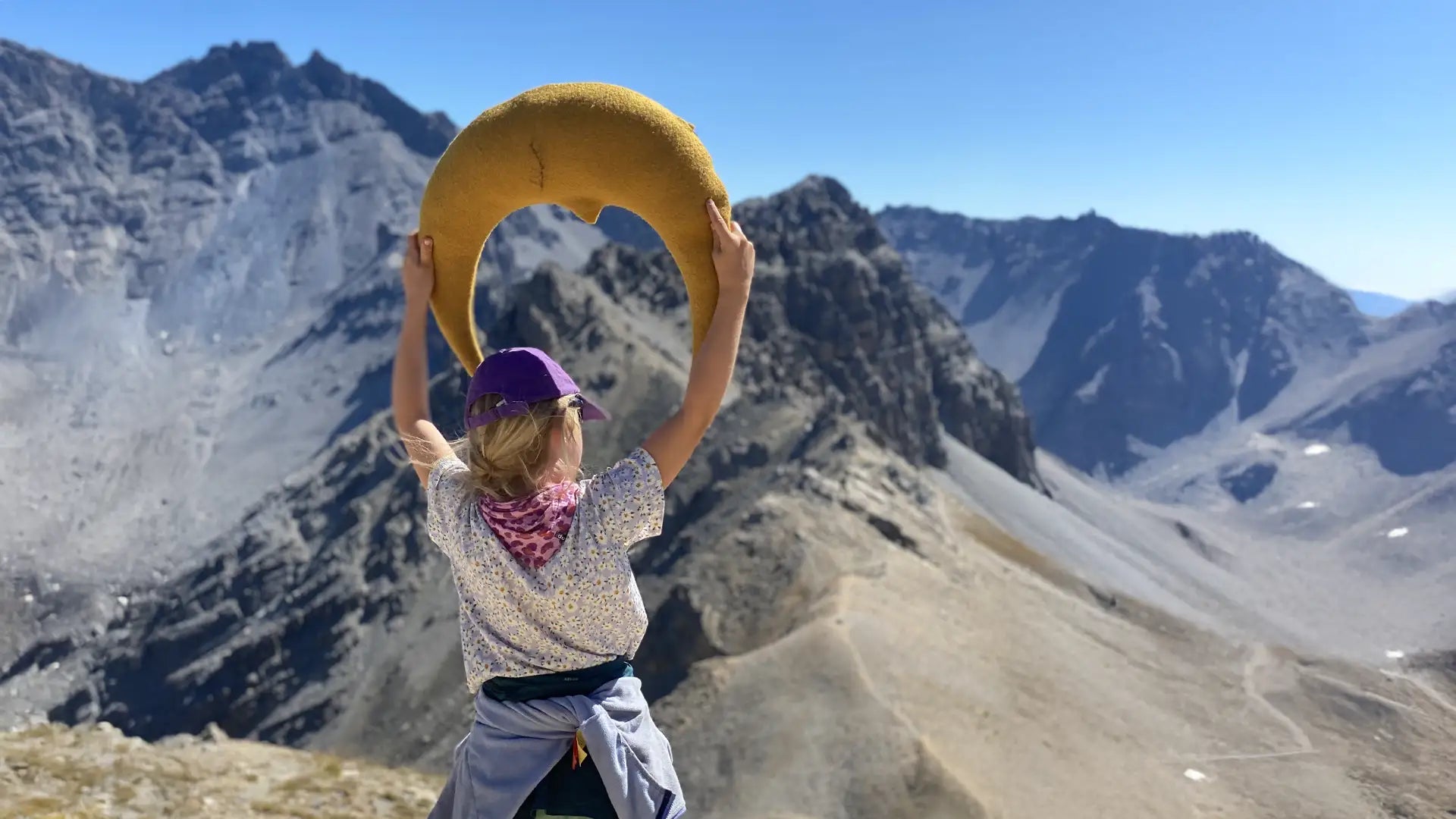 Kind mit großem Mondkissen in Goldgelb blickt Richtung Bergpanorama in den Alpen