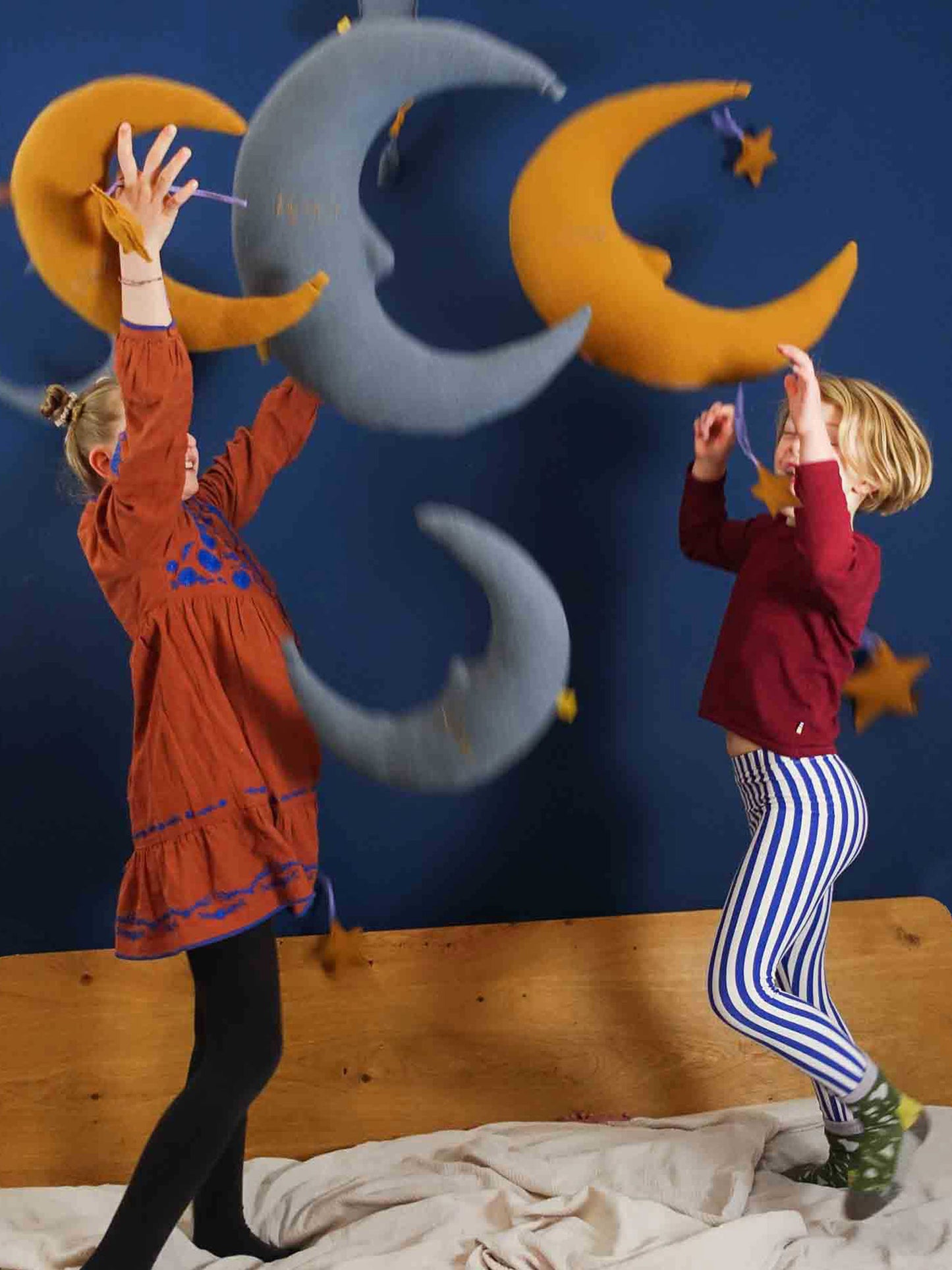 blaue und gelbe Kissen in Mond- und Sternform werden von zwei Kindern im Spiel nach oben geworfen